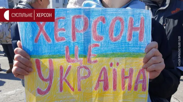 A person holds a sign with Ukrainian lettering that translates as 'Kherson is Ukraine'