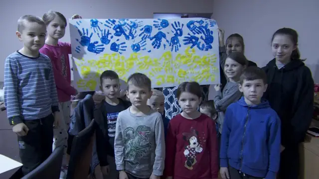 Children hold up a Ukrainian flag made from hand prints