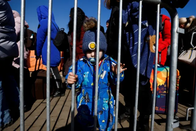 A Ukrainian child stands behind the barrier while queuing with his family to get into the bus at the border checkpoint in Medyka, Poland