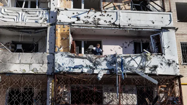 Woman cleans debris from her apartment inside a residential building after it was hit by shelling in Kyiv