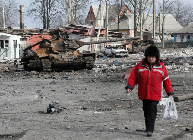 A woman walks passed a destroyed tank in Volnovakha, in the Donetsk region