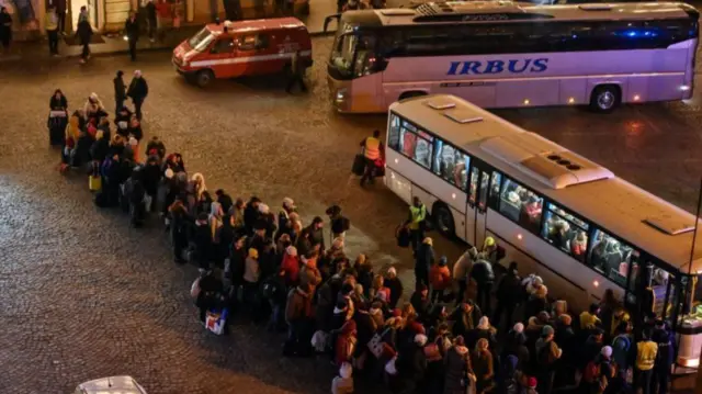 Ukrainian refugees in Poland queue for a coach to carry them to other parts of the country