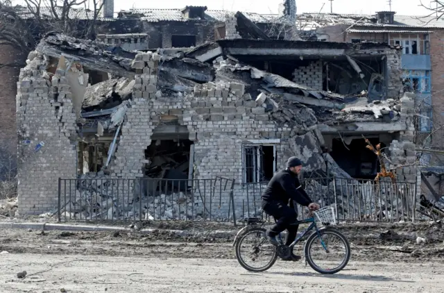 A man rides a bicycle past a damaged building in Volnovakha, in the Donetsk region