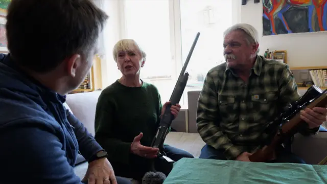 Lesya and Yuri Voloshchak sitting in their house holding their rifles