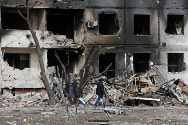 A man walks near a block of flats in Mariupol, destroyed by shelling