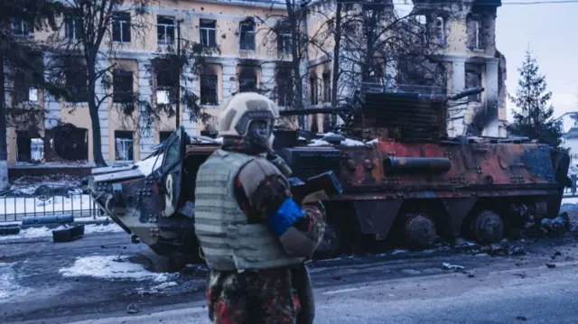 A Ukrainian soldier passes a destroyed armoured vehicle in Kharkiv