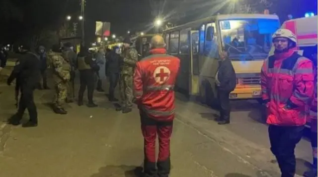 Rescuers and officers in fatigues help usher fleeing civilians onto waiting buses leaving the Kyiv region