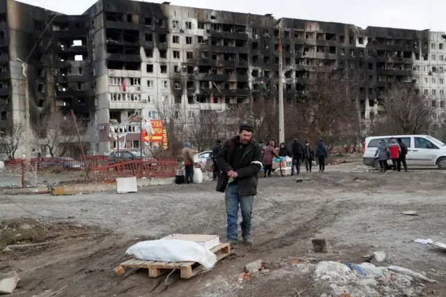 People gather near a destroyed block of flats in besieged Mariupol