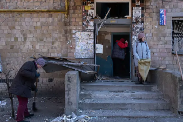 Women cleaning up shattered glass pieces of their residential building