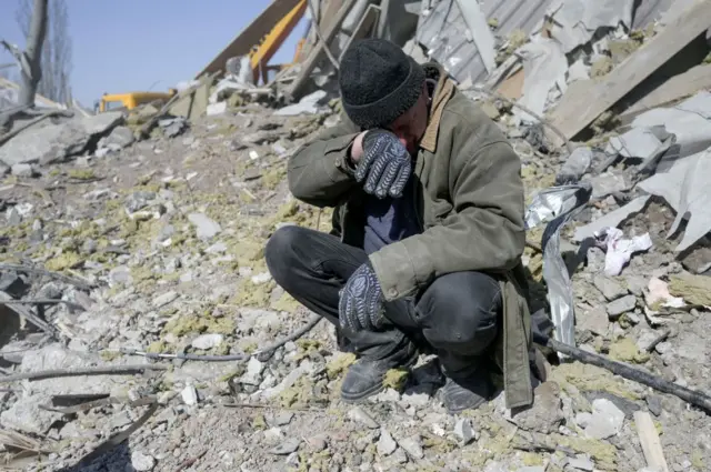 A man helps Ukrainian soldiers searching for bodies in the debris at the military school hit by Russian rockets the day before, in Mykolaiv, southern Ukraine