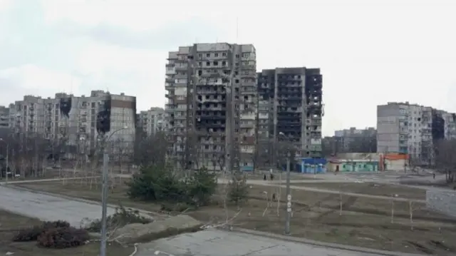 Damaged residential buildings and a road block in the besieged city of Mariupol