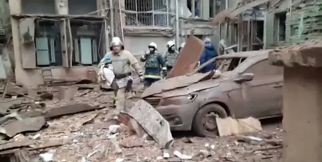 Emergency service personnel stand among debris in Kharkiv