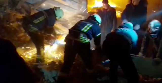 Rescuers in protective fire gear working to remove people from a fiery blast