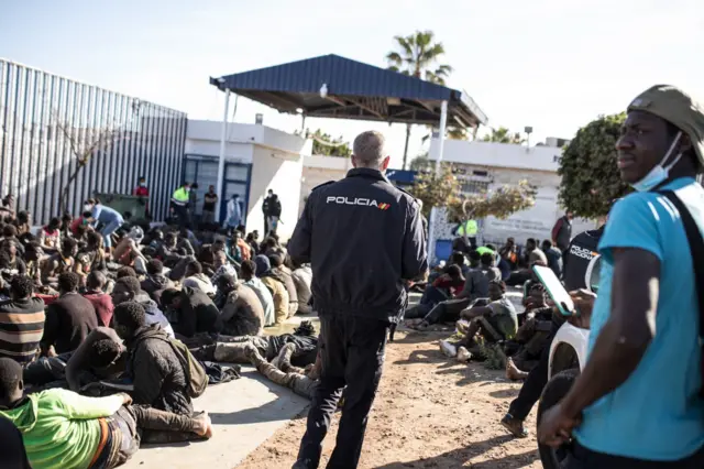 Spanish policeman in yard with African migrants