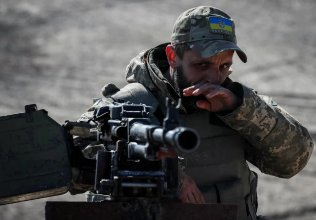 A Ukrainian service member stands near a machine gun on the front line in the east Kyiv region