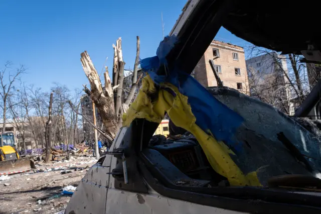 A torn Ukraine flag is seen at a destroyed car in Kyiv