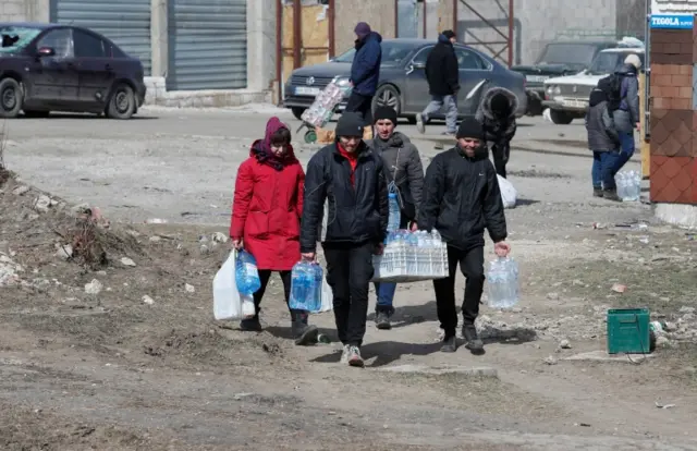 Local residents carry bottles with water in the besieged city of Mariupol 20 March 2022