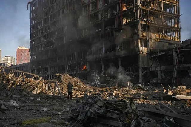 A man stand looking at the burning and destroyed Retroville shopping mall after a Russian attack on the north-west of the capital, Kyiv, on 21 March 2022