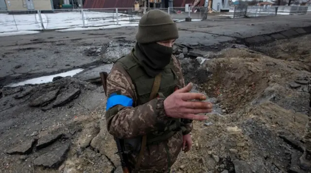 A Ukrainian service member stands next to a bomb crater in the town of Okhtyrka