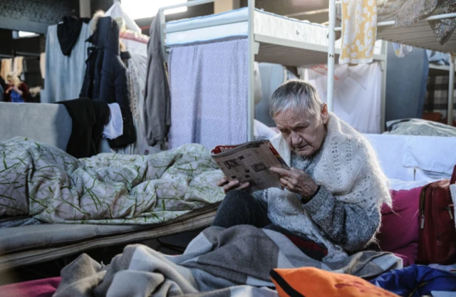 An old woman reads at a gym converted for accommodation for refugees in Lviv