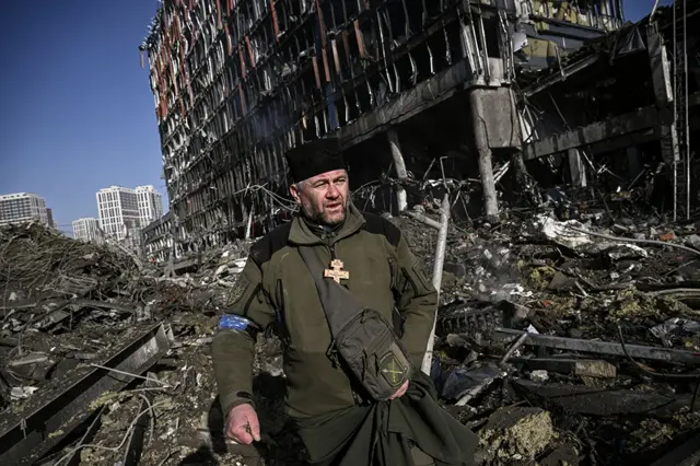 Ukraine army chaplain Mikola Madenski walks through debris outside the destroyed Retroville shopping mall in a residential district after a Russian attack on the Ukranian capital Kyiv on 21 March 2022