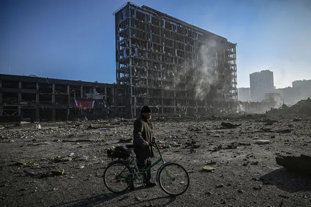 A man with his bicycle walks between debris outside the destroyed Retroville shopping mall in a residential district, after a Russian attack on the Ukranian capital, Kyiv, on 21 March 2022