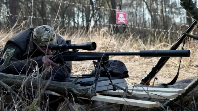 A trainee lies prone, aiming his sniper rifle at the targets