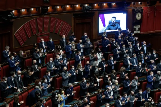 Members of the Italian Parliament give Ukraine's President Volodymyr Zelensky (on screen) a standing ovation at the end of his speech to members of the Italian Parliament via video link in Rome, Italy, on 22 March 2022