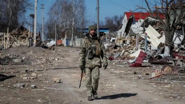 Ukrainian service member walks in a destroyed village on the front line in the east Kyiv region