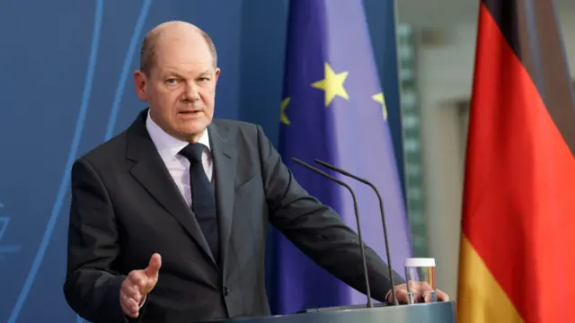 German Chancellor Olaf Scholz addresses the media in front of the EU and German flags