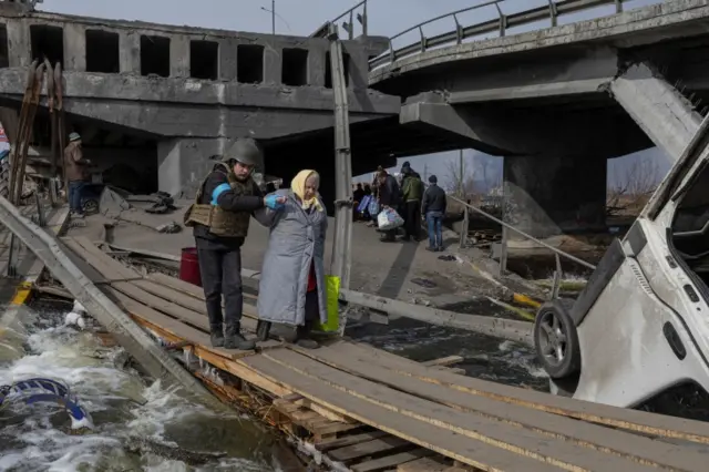 Woman crosses makeshift bridge to leave Irpin, Ukraine