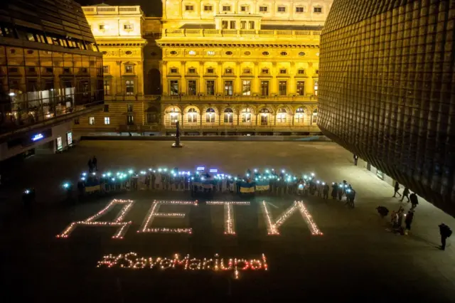 People holding flags and shining lights from their mobile phones pose next to candle lightings reading "Children , save Mariupol' during a rally against Russia's invasion of Ukraine on March 22, 2022 in Prague.