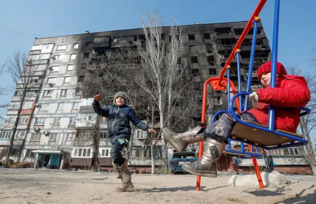 Children play in front of a building damaged in fighting during Ukraine-Russia conflict, in the besieged southern port of Mariupol, 23 March 2022