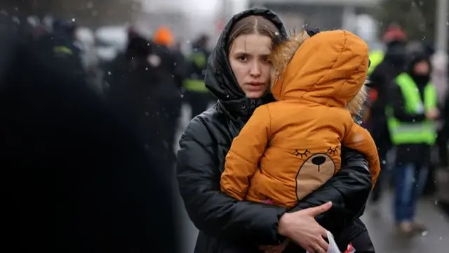 Woman carrying a child at a border crossing after fleeing Ukraine