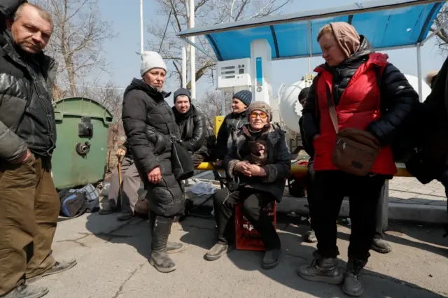 Evacuees in hats and coats wait for a bus out of embattled Mariupol on Thursday