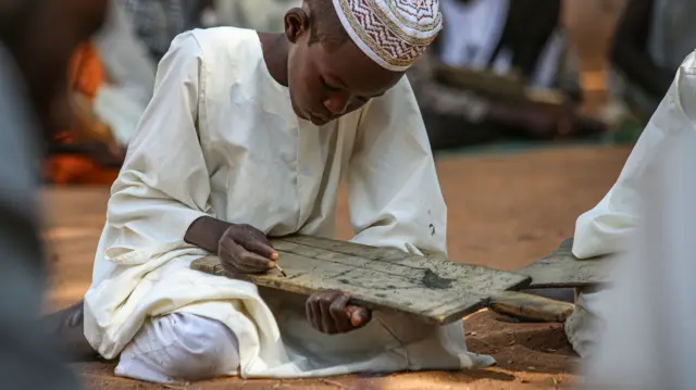 A boy holding a wooden board in a Quranic school