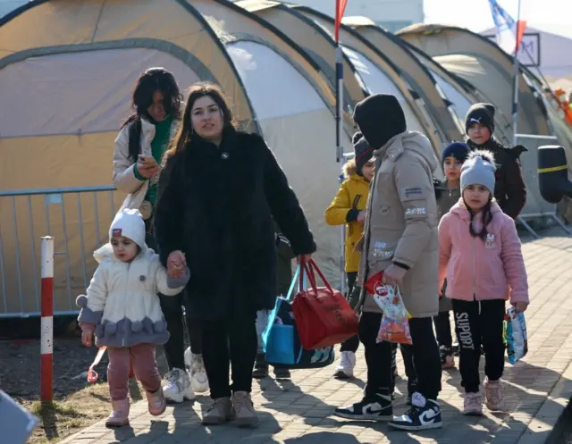 People walk beside tents after crossing the border from Ukraine to Poland, fleeing the Russian invasion of Ukraine, at the border checkpoint in Medyka, Poland,