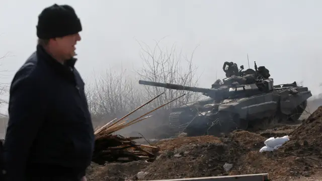 Man walks along a road past a tank on outskirts of the besieged city of Mariupol