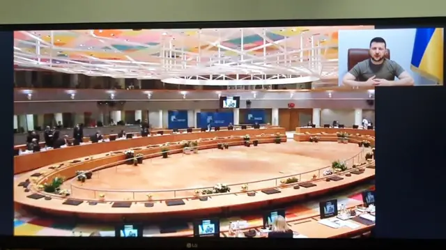 Split screen shows the European Council members in a chamber listening to a speech from Ukraine leader Zelensky