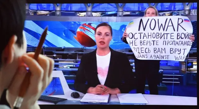 A woman looks at a computer screen watching a dissenting Russian Channel One employee entering Ostankino on-air TV studio during Russia's most-watched evening news broadcast