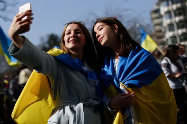 Women wrapped in Ukrainian flags take a selfie during a demonstration in support of Ukraine