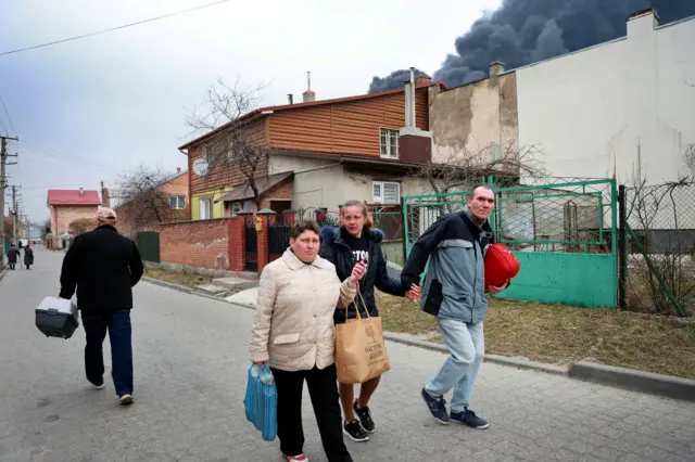 People in Lviv walk under a plume of black smoke