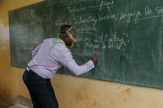 A teacher wearing a face shield as a preventive measure against the spread of the COVID-19 coronavirus writes on the board at the Technical High School of Nkol-Bisson in Yaoundé, Cameroon, on June 1, 2020.