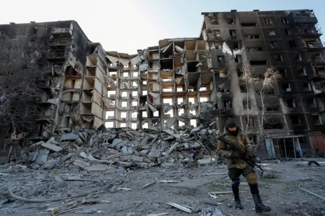 A service member of pro-Russian troops walks near an destroyed apartment building in Mariupol