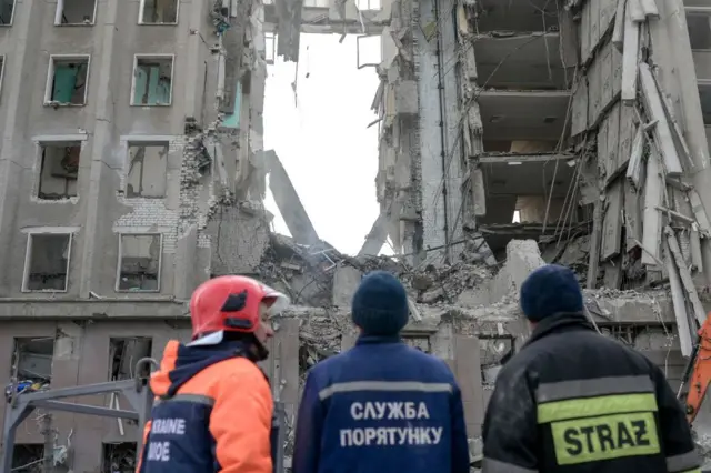 Emergency service workers look at a destroyed administrative building in Mykolaiv