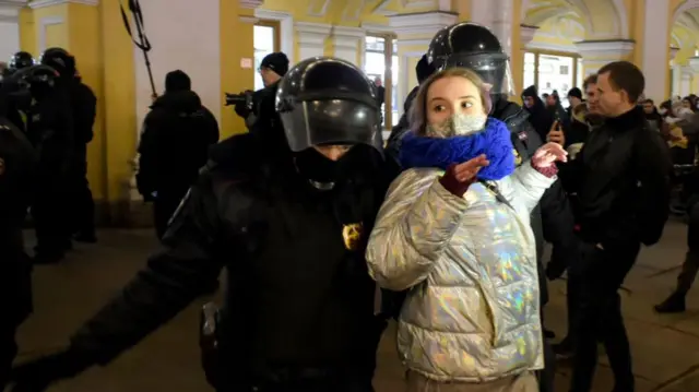 A young woman with her hands up is escorted away by two police officers in Saint Petersburg