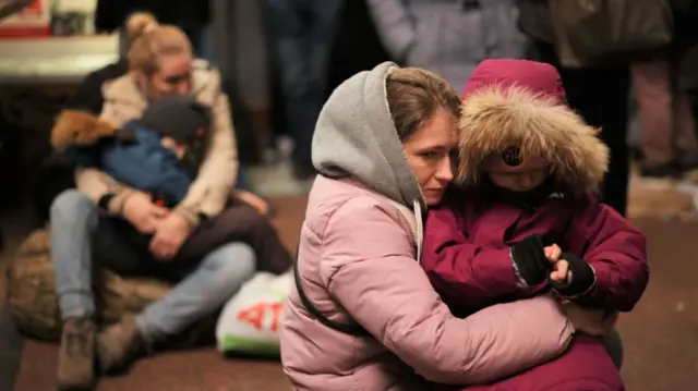 Two women in Lviv hug their children while waiting to board a train to Poland