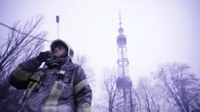 A firefighter stands with his phone to his ear in front of Kyiv's TV tower