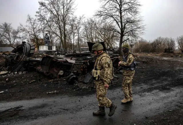 Ukrainian soldiers and a destroyed Russian vehicle near Kyiv on 30 March