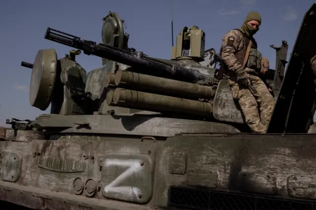 A Ukrainian soldier sits on top of a captured Russian artillery vehicle near Kharkiv